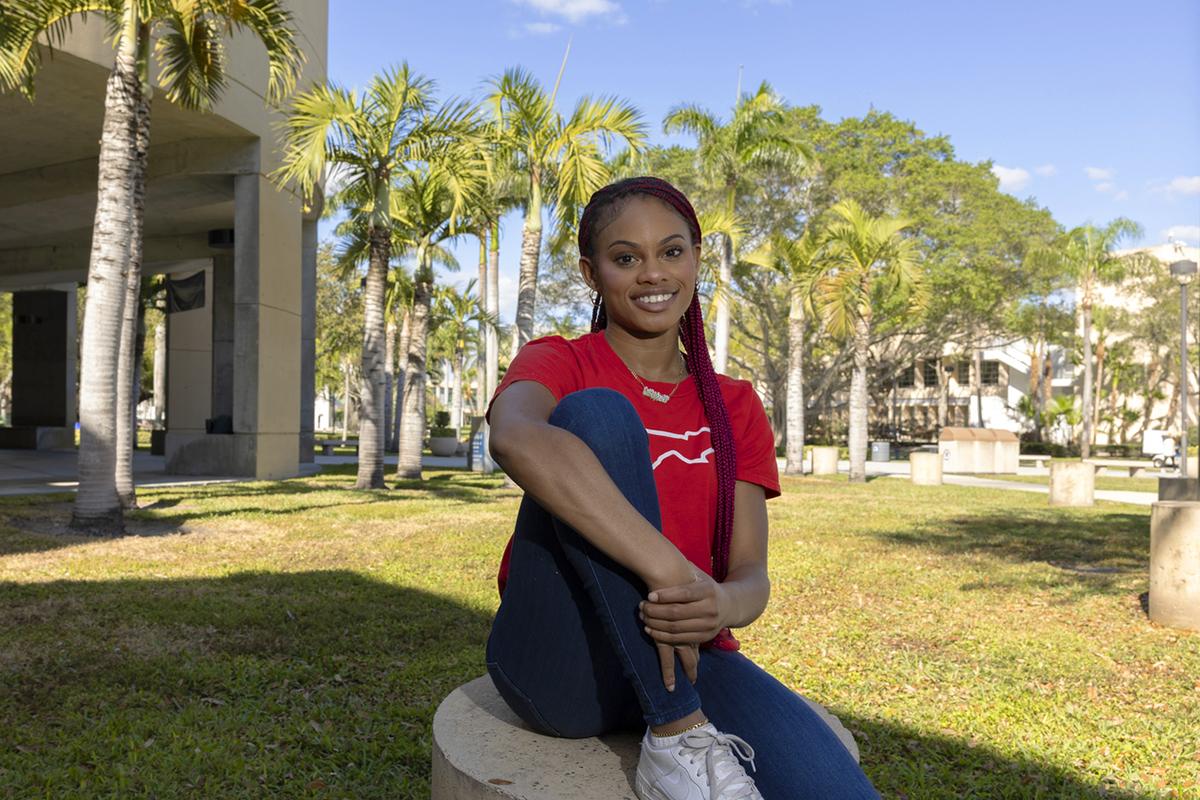 A student sitting on a short pillar and smiling at the camera